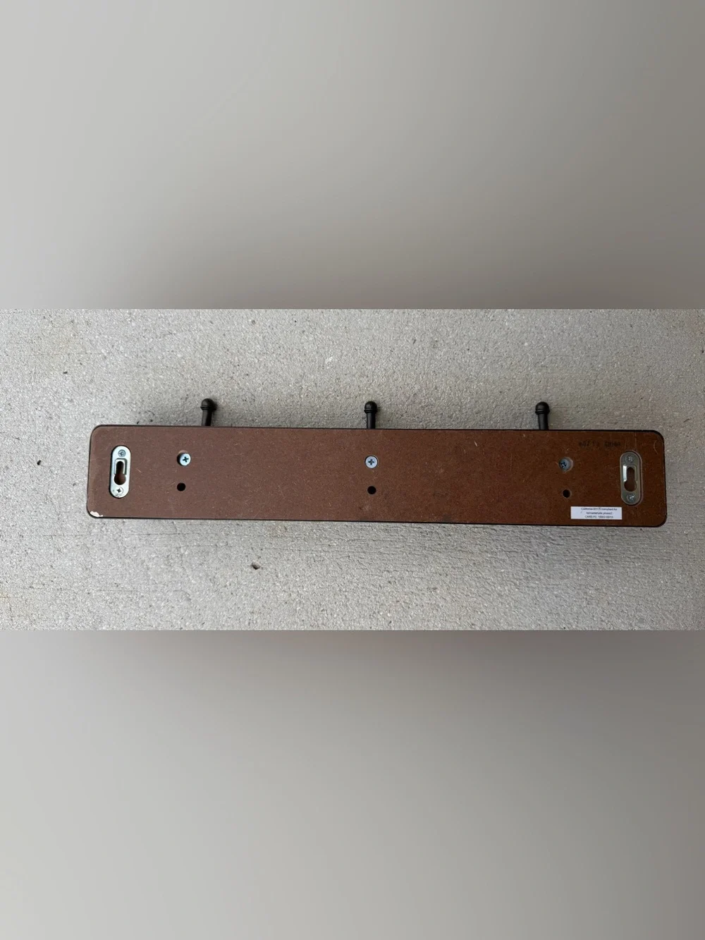 Hook rack features a dark bronze frame with a light-colored linen backing